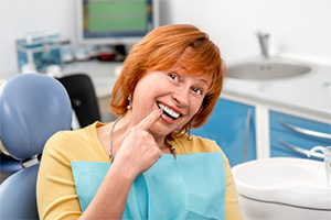 Older woman in dental chair pointing to smile