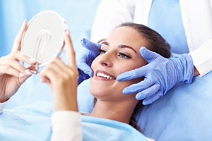 woman smiling at hand mirror while sitting in dental chair 