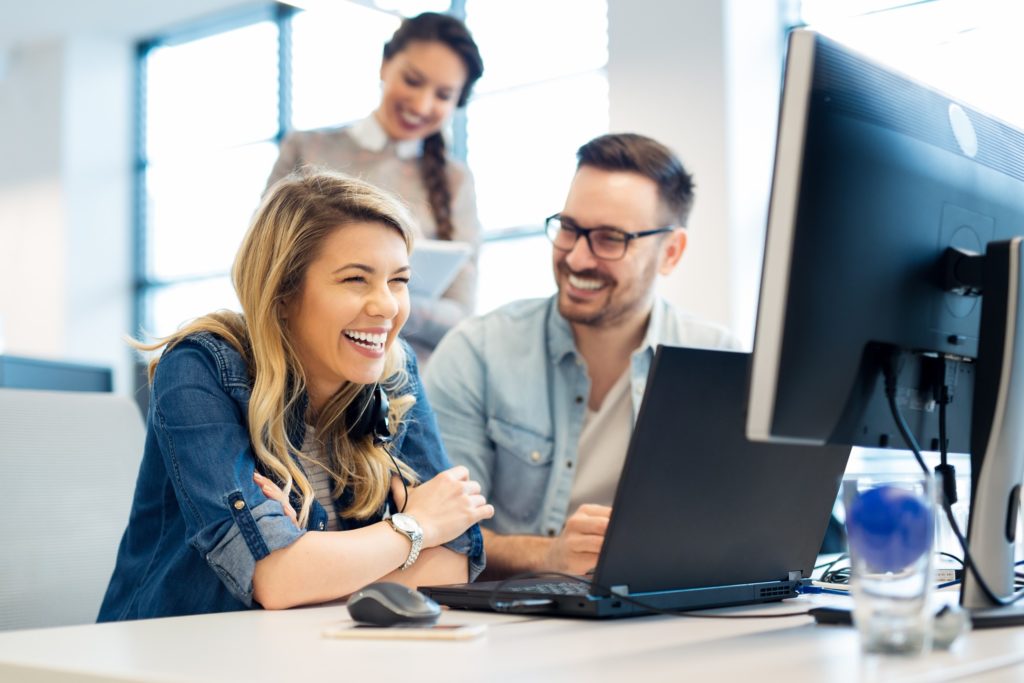 Group of colleagues smiling while working on computer at office