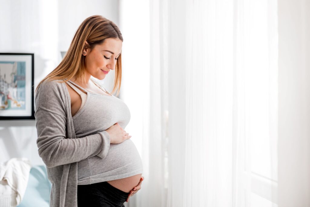 Woman in gray shirt looking down at pregnant belly