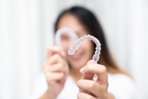 Woman smiling while holding up her Invisalign trays